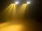 Bühne mit gelbem Scheinwerferlicht im Nebel. Vier helle Lichter strahlen von oben auf eine leere Fläche.