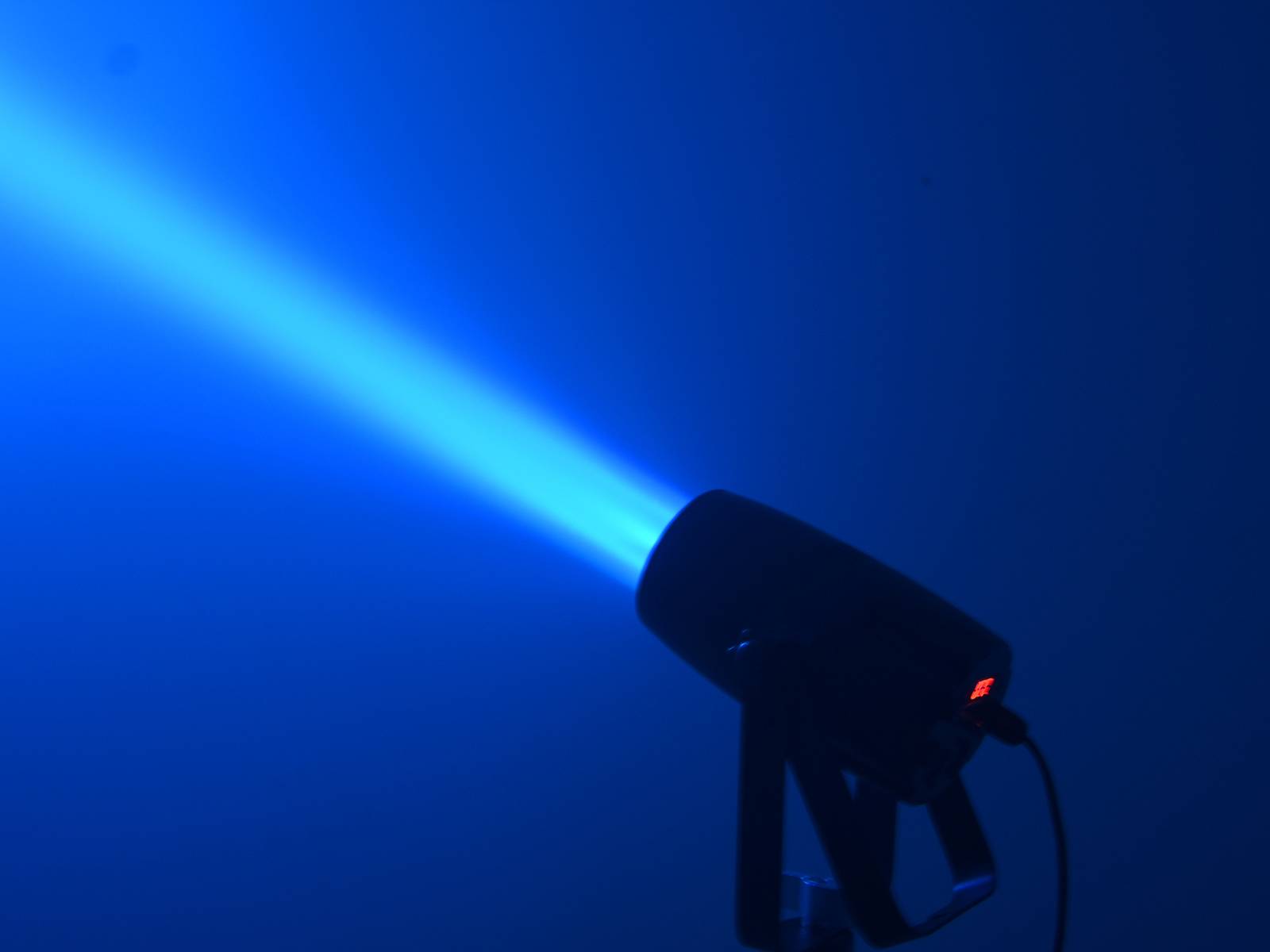 Ein Scheinwerfer strahlt einen hellblauen Lichtstrahl in einen dunklen Raum aus.