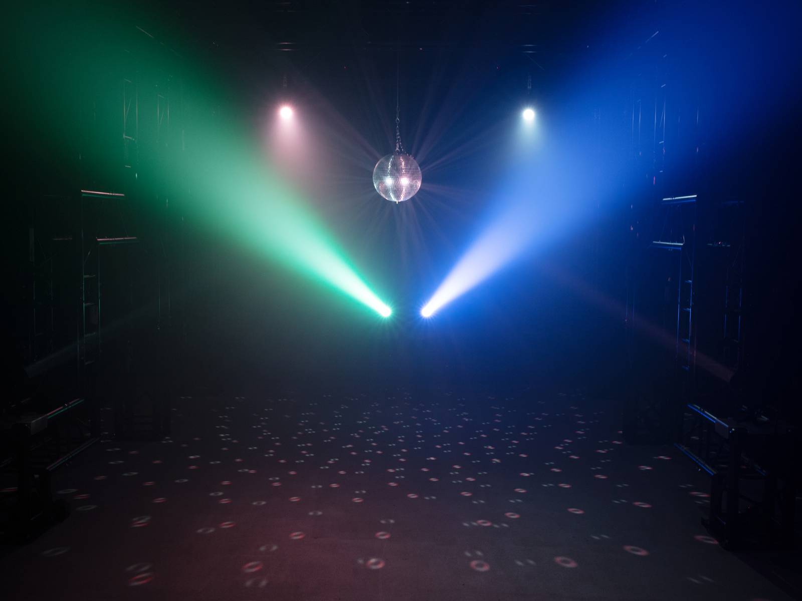 Eine Disco-Kugel in einem dunklen Raum reflektiert farbiges Licht in Grün, Rot und Blau, erzeugt Muster auf dem Boden.