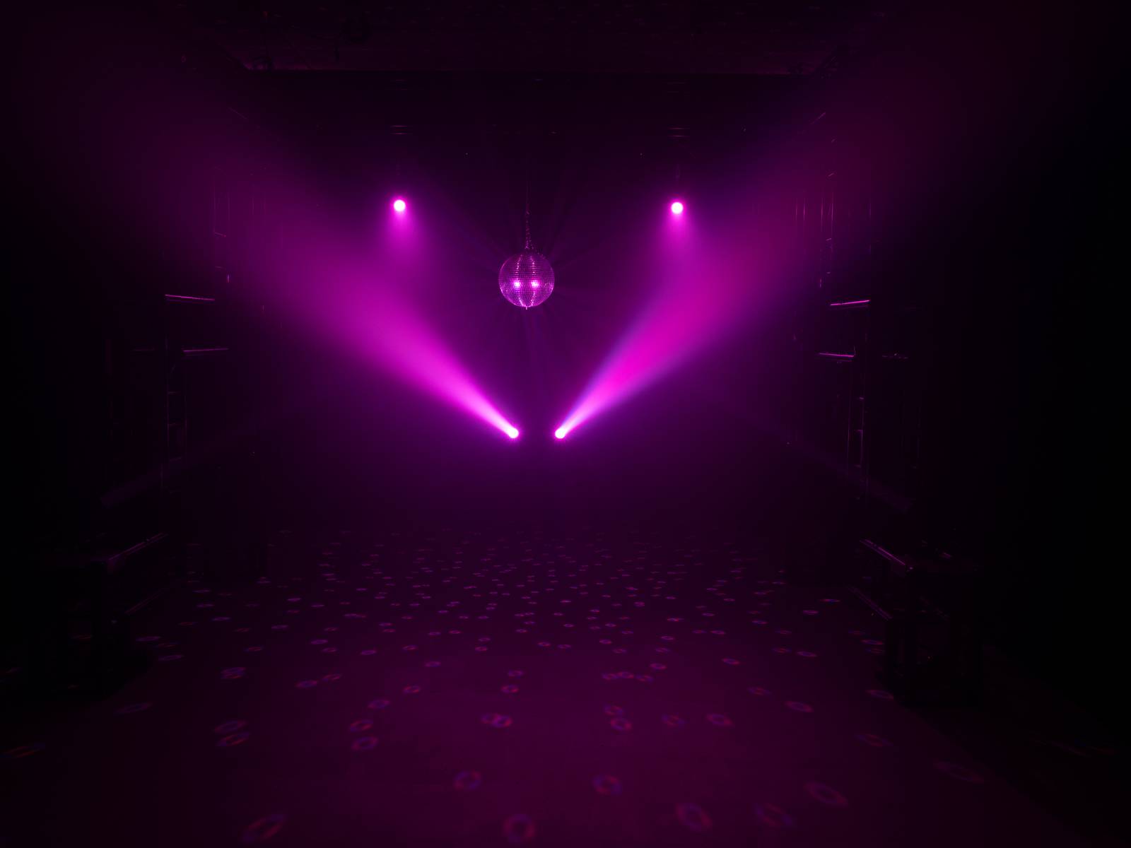 Eine dunkle Diskothek beleuchtet mit rosa Scheinwerfern, einer Glitzerkugel in der Mitte, die Lichter und Reflexionen auf den Boden wirft.