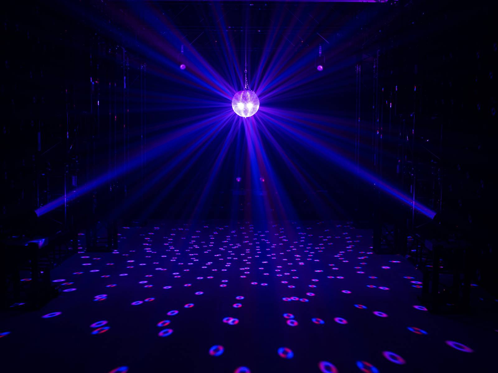 Tanzfläche mit Discokugel in der Mitte, reflektiert farbige Lichter. Umgebung dunkel, stimmungsvolles Partyambiente.