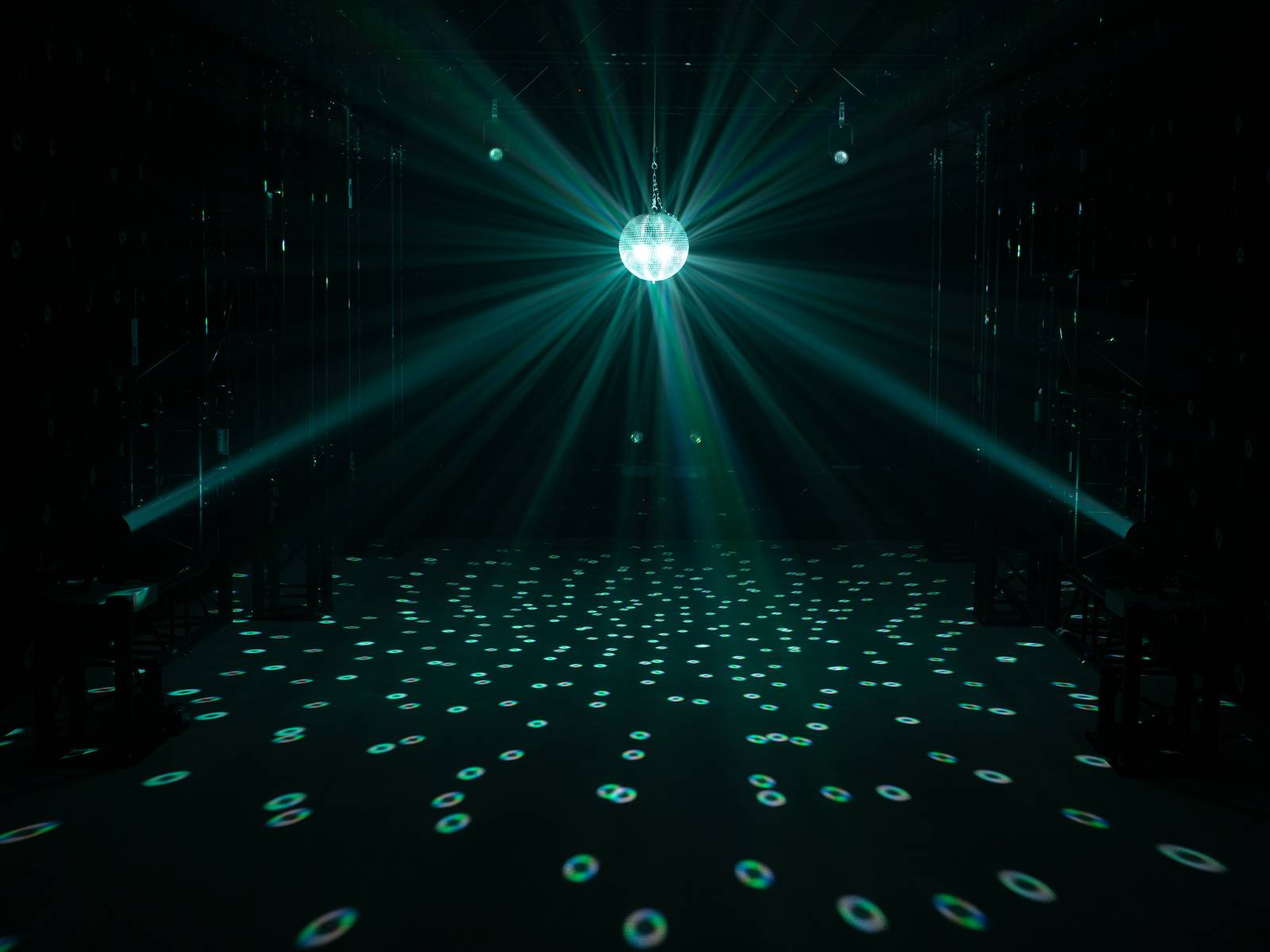 Eine Discokugel hängt über einer dunklen Tanzfläche, auf der Lichtpunkte verteilt sind, die durch die reflektierenden Strahlen entstehen.