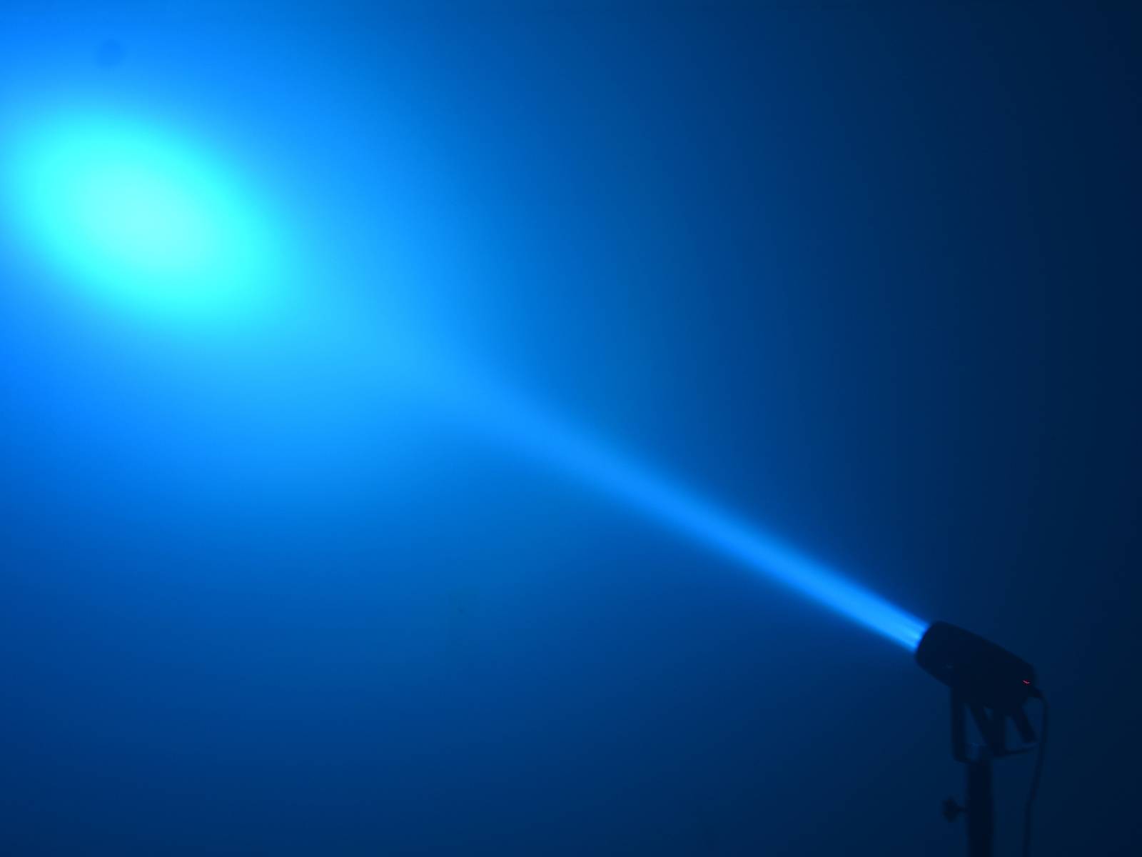 Ein blauer Scheinwerfer strahlt in einem dunklen Raum, erzeugt einen gerichteten Lichtkegel und beleuchtet einen Bereich intensiv.