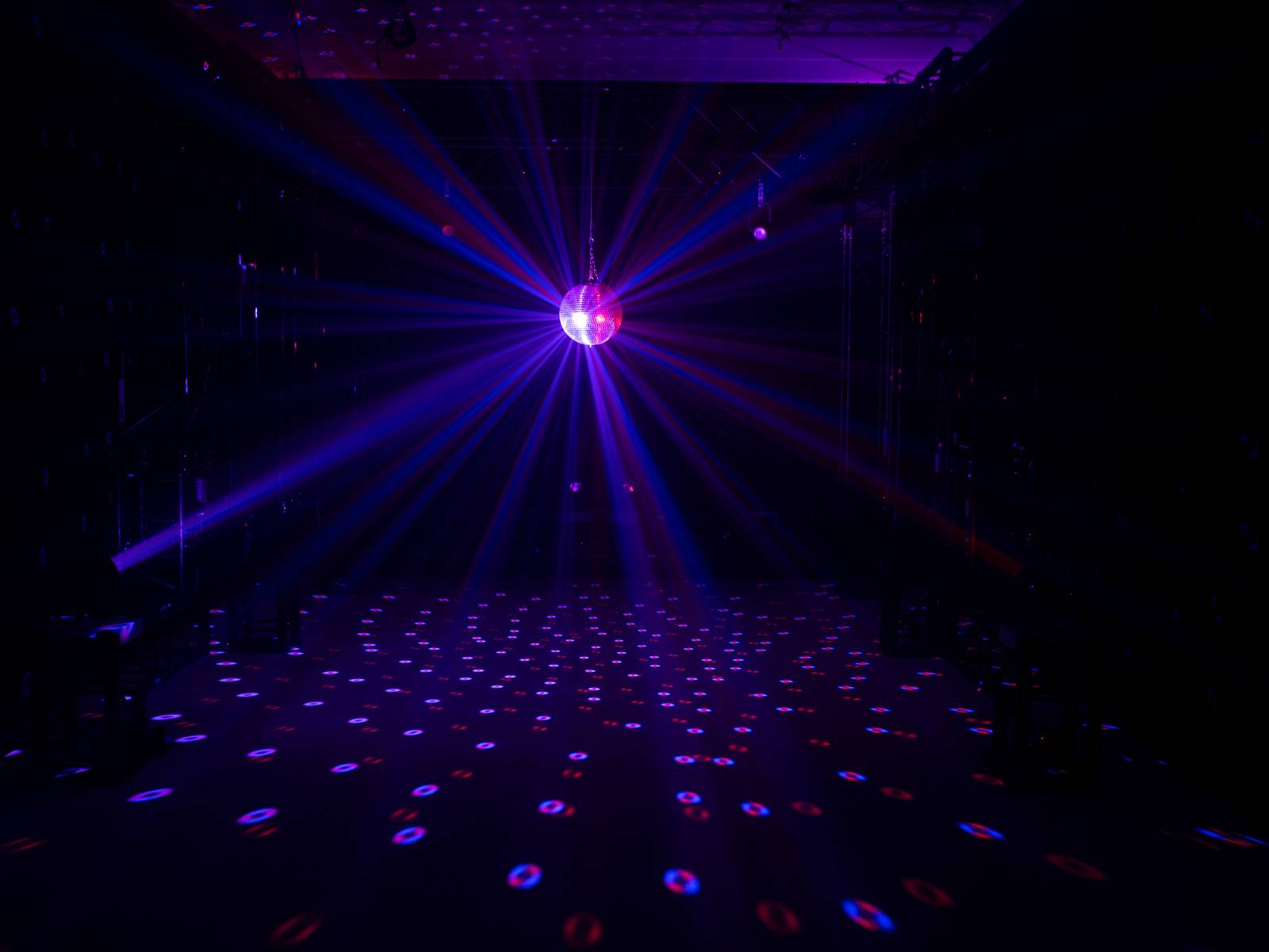 Eine Discokugel hängt in einem dunklen Raum und wirft bunte Lichter und Muster auf den Boden.