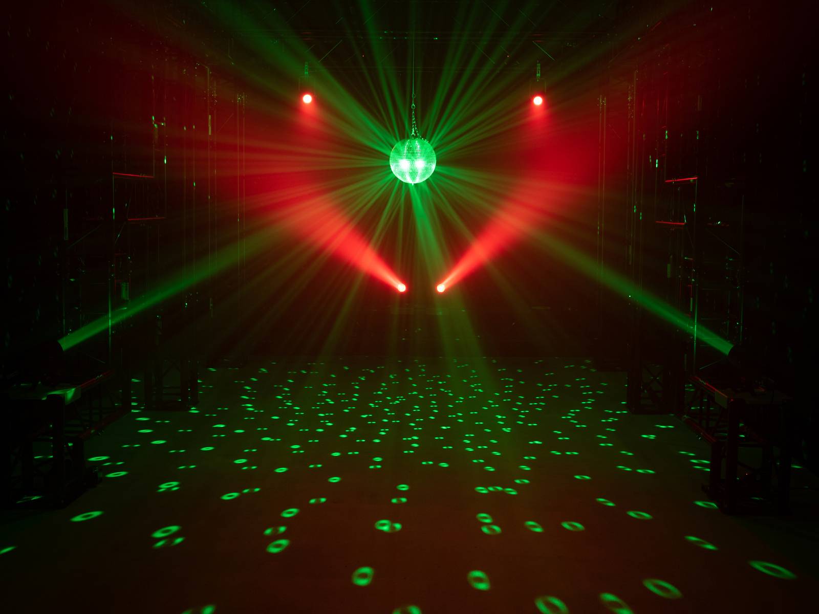 Diskokugel strahlt bunte Lichter in einem dunklen Raum aus. Rote und grüne Lichtstrahlen erzeugen eine dynamische Atmosphäre.