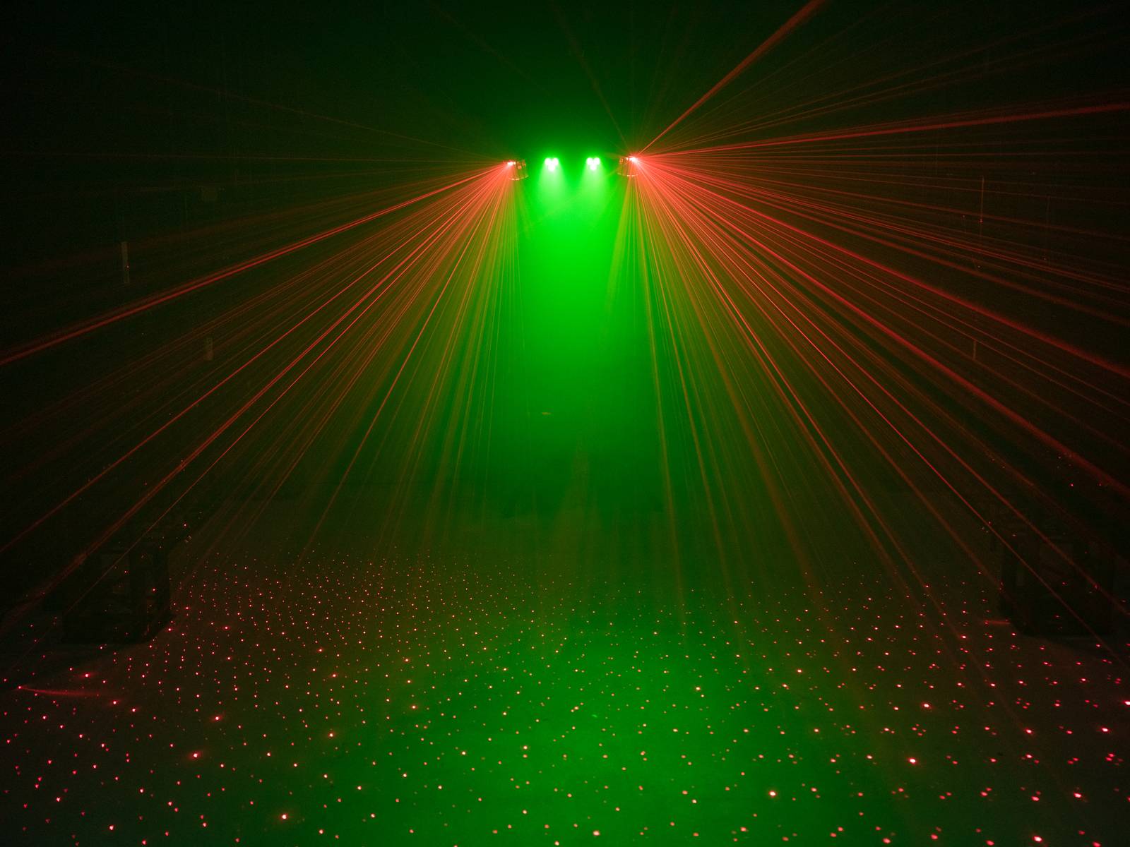 Grünes und rotes Laserlicht, das in einem dunklen Raum strahlt und ein komplexes Muster auf dem Boden erzeugt.