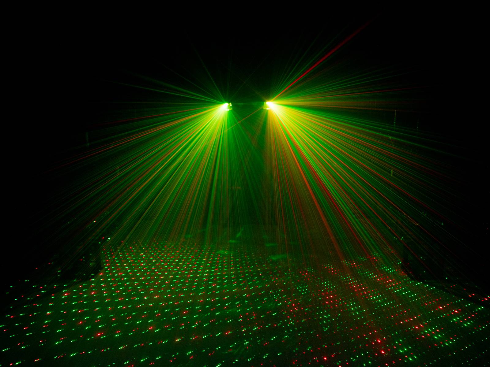 Grüne und rote Laserstrahlen erzeugen ein geometrisches Muster auf einer dunklen Fläche.