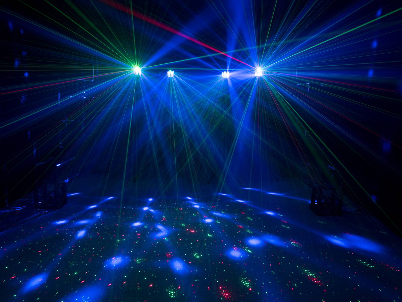 Lichteffekte in einem dunklen Raum, mit bunten Laserstrahlen, die über die Tanzfläche hinweg leuchten und eine lebendige Atmosphäre schaffen.