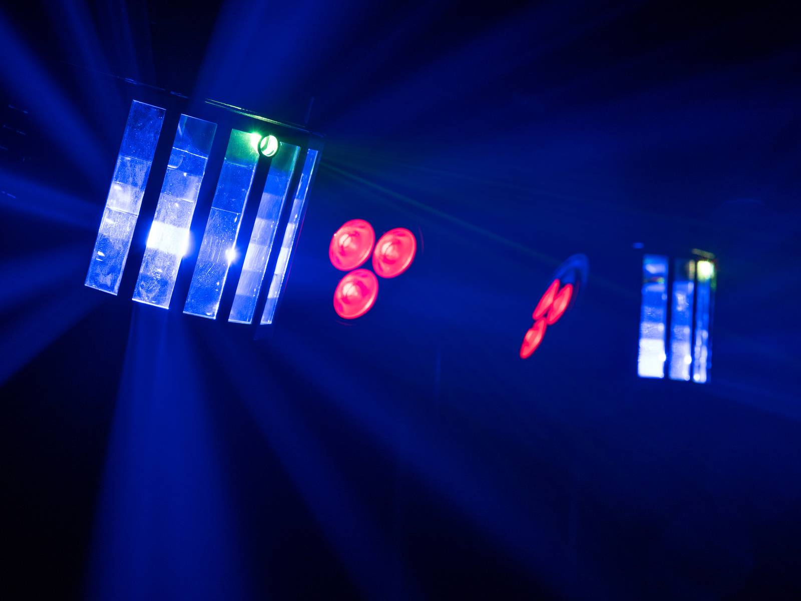Blaue und rote Lichter leuchten in dunkler Umgebung, erzeugen Strahlen und Muster, die auf eine Bühnenbeleuchtung hindeuten.