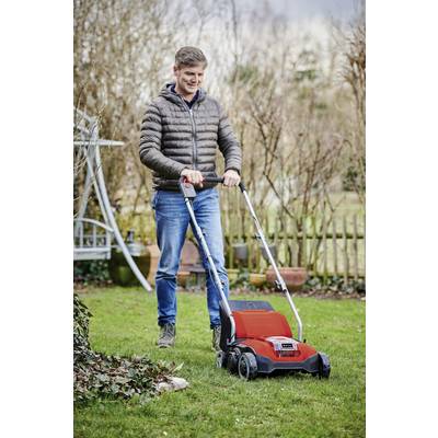 Ein Mann in Freizeitkleidung schiebt einen roten Rasenmäher über einen grünen Rasen in einem Garten mit Holzzaun und kahlen Sträuchern.