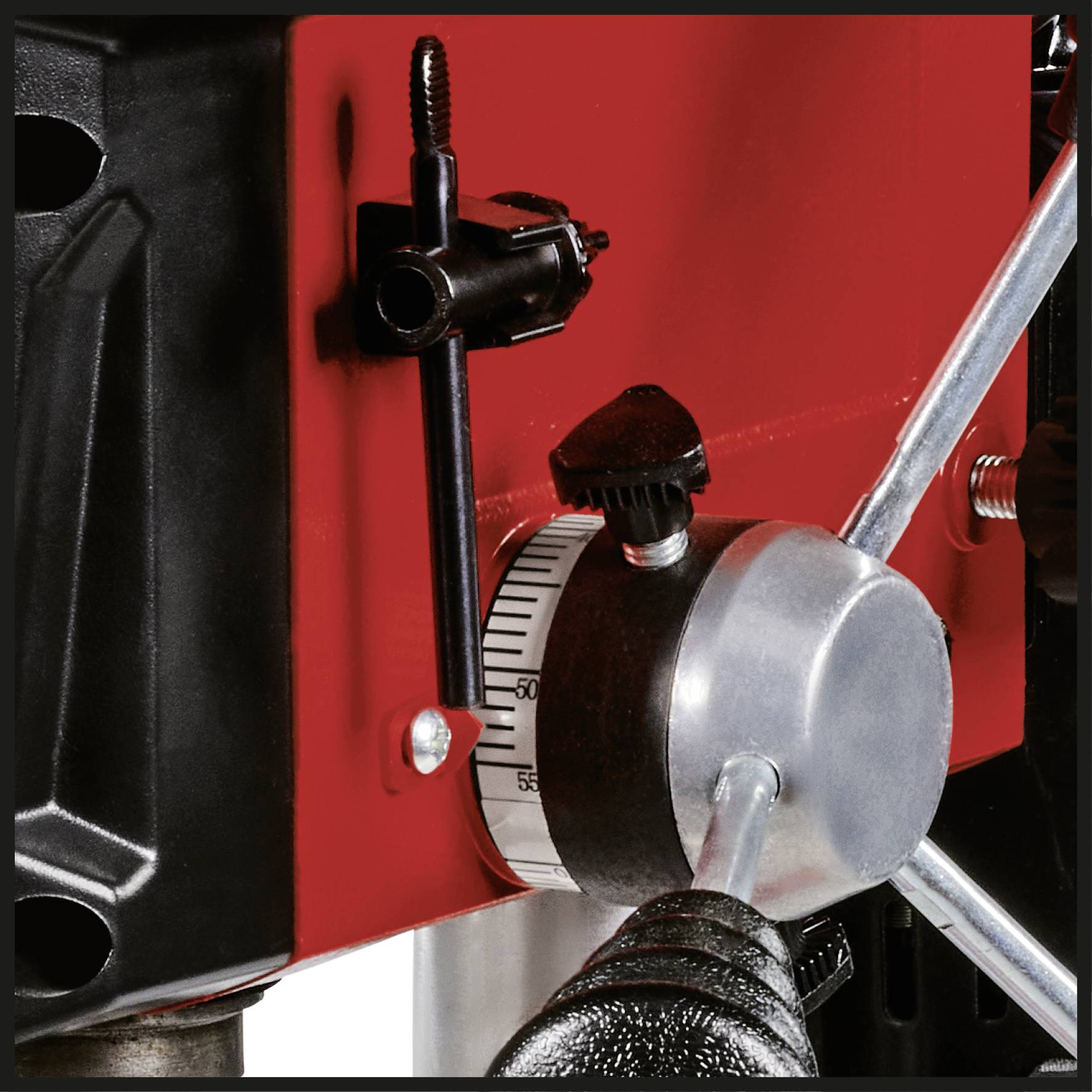 Nahaufnahme einer drehbaren Metallskala an einer Maschine, wahrscheinlich für präzise Einstellungen. Roter Hintergrund, schwarze Klemme sichtbar.