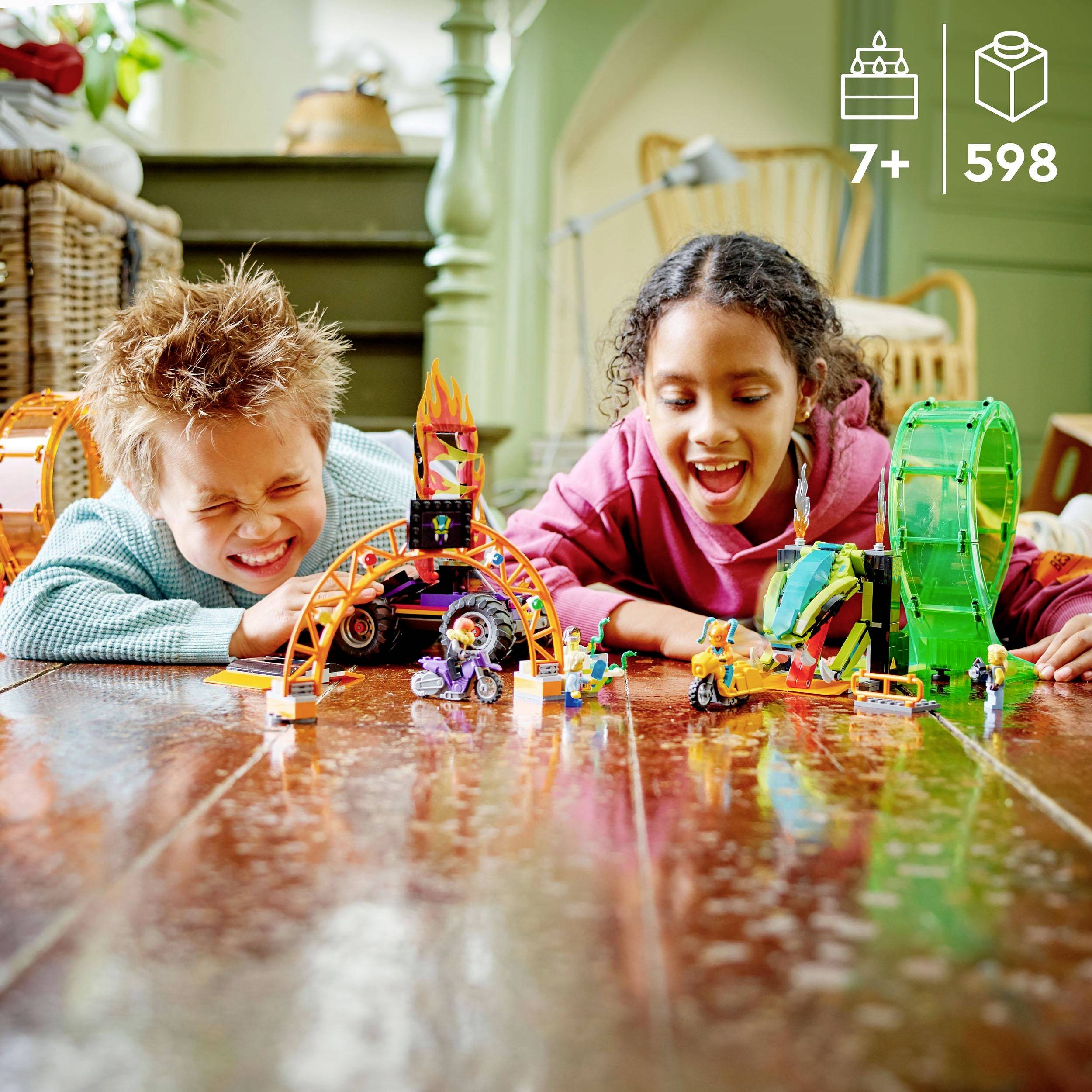 Zwei lachende Kinder spielen auf dem Holzboden mit bunten Bausteinen und LEGO-Spielzeug. Im Hintergrund ist ein gemütliches Wohnzimmer.
