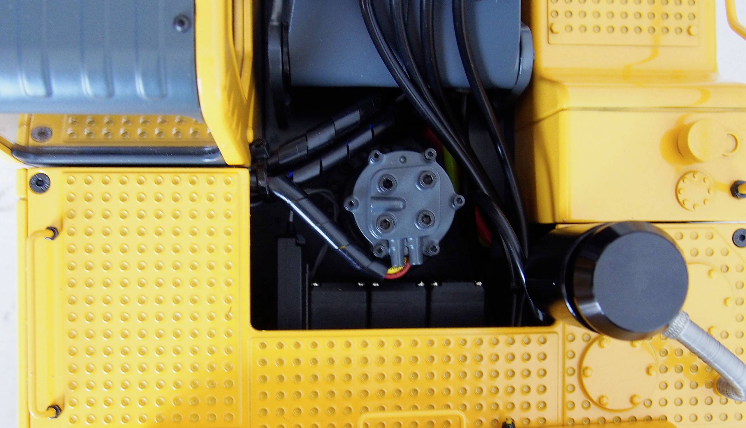 Detailaufnahme eines gelben Spielzeugbaggers mit sichtbarem Maschinenraum und Kabeln, von oben betrachtet.