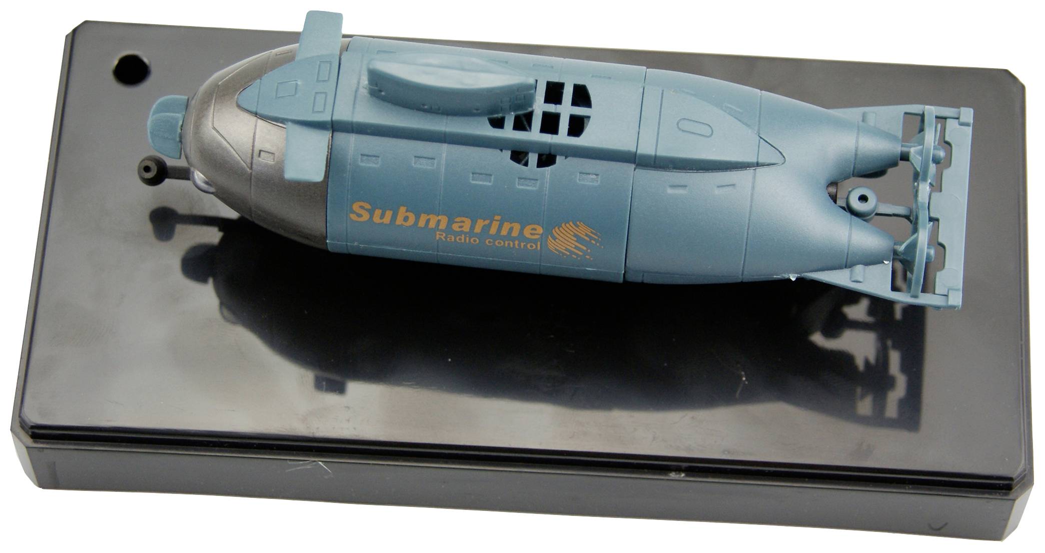 Spielzeug-U-Boot mit Fernsteuerung, grün-blau, auf schwarzem Sockel. Schriftzug 'Submarine Radio Control' sichtbar.