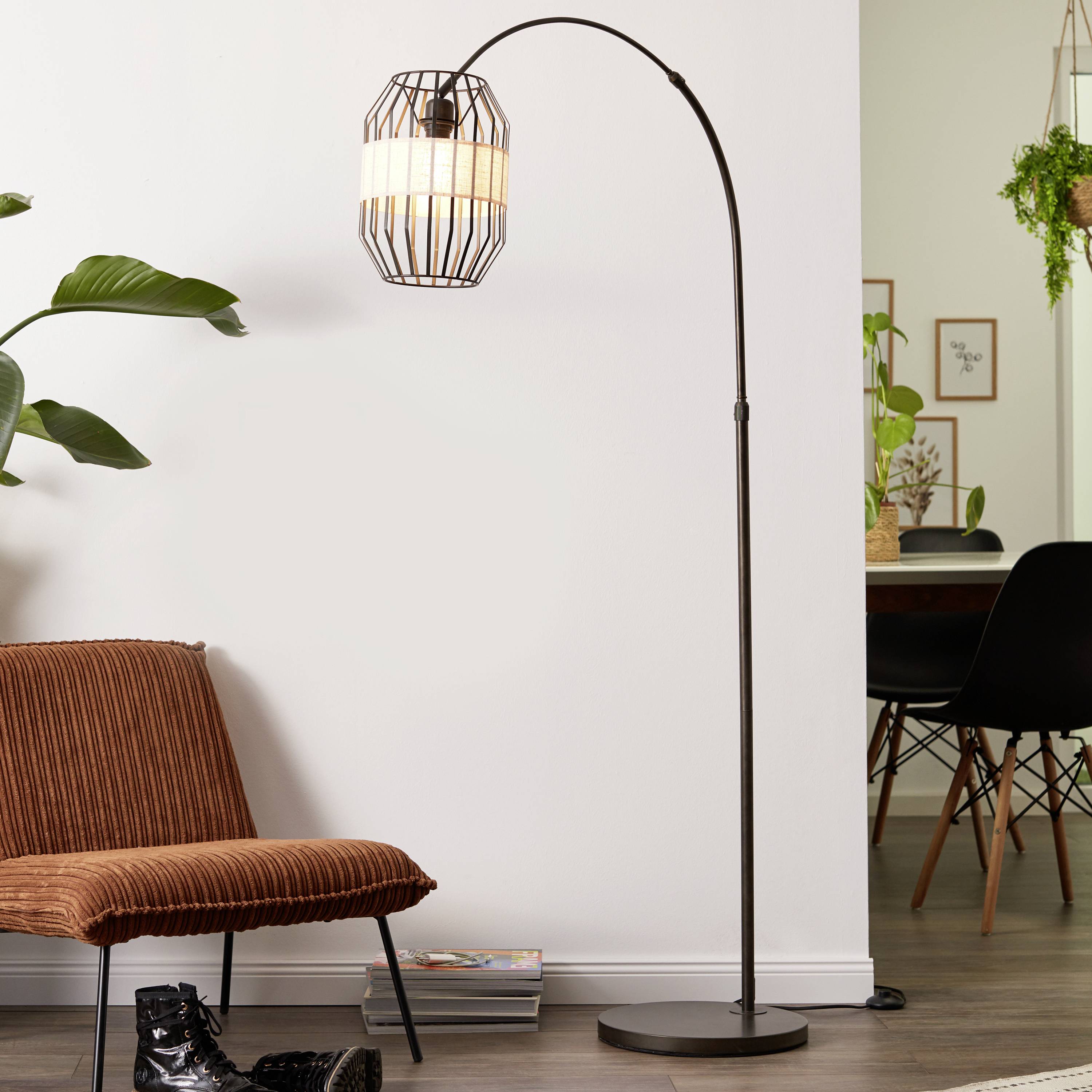 Eine schwarze Stehlampe mit einem hängenden, gestreiften Lampenschirm steht neben einem braunen Sessel in einem modernen Wohnzimmer.