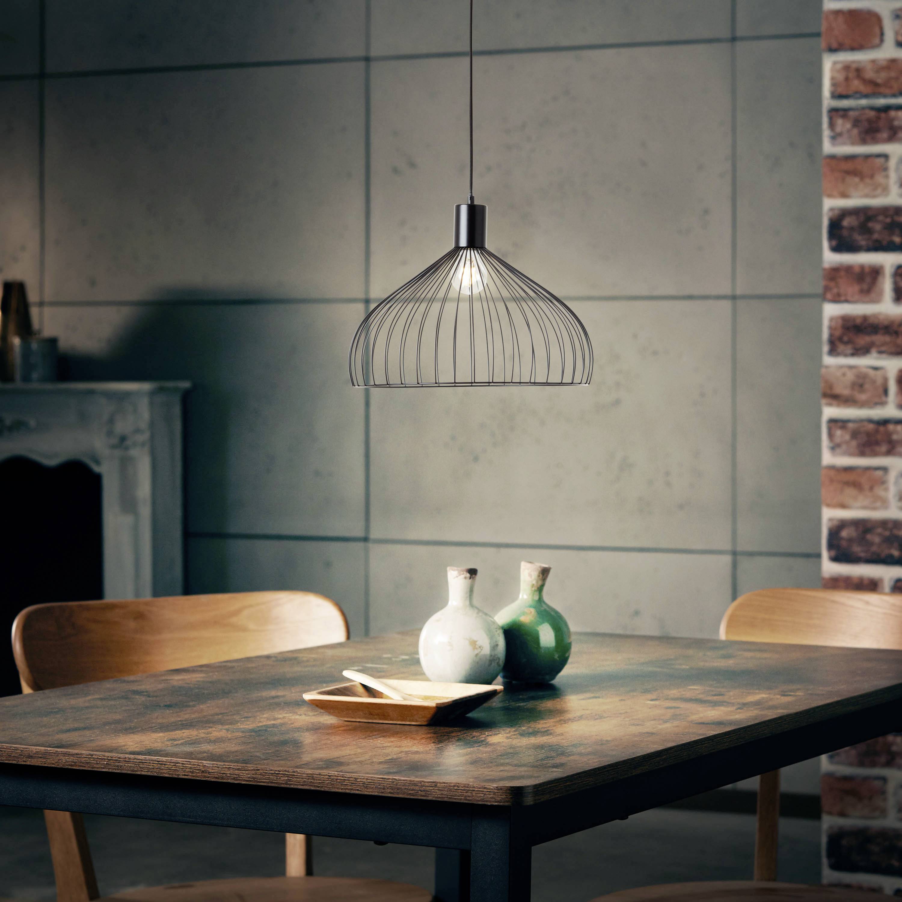 Holztisch mit grüner und weißer Vase, Teller. Hängelampe über dem Tisch. Stühle und dekorative Ziegelwand im Hintergrund.