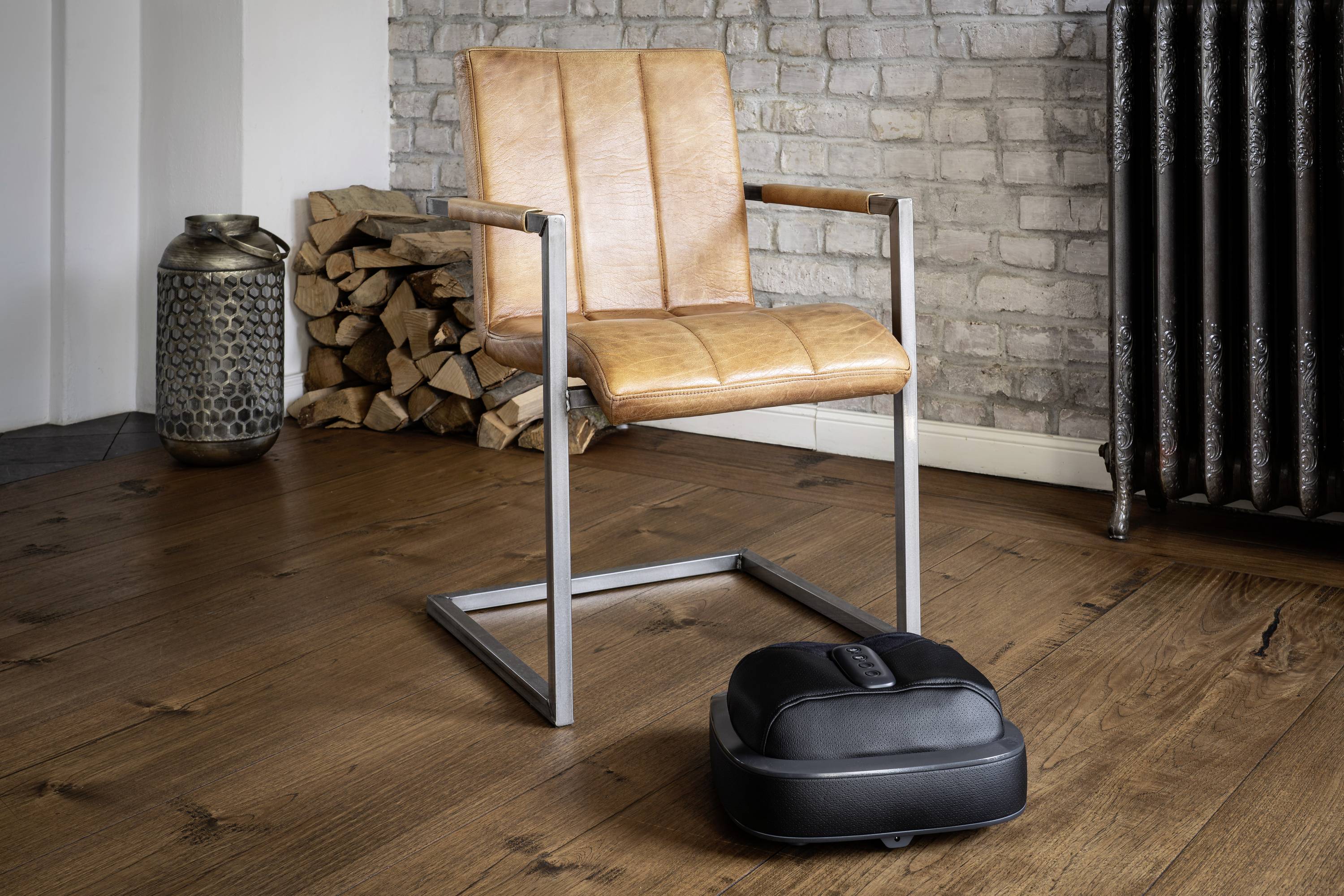 Brauner Lederstuhl auf Holzboden, daneben ein schwarzer Saugroboter. Hintergrund: gestapelte Holzscheite und dekorative Vase.