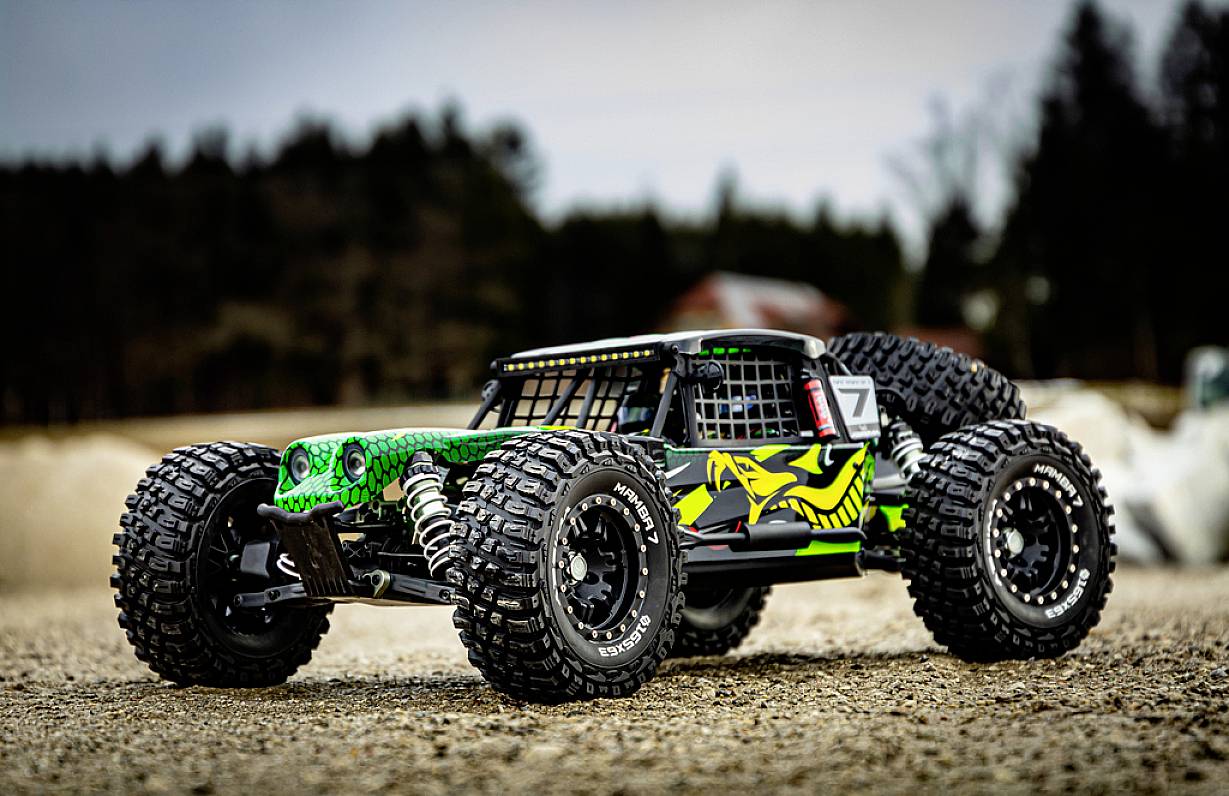 Ein ferngesteuertes Auto im Offroad-Design mit großen Reifen steht auf einer kiesbedeckten Fläche; Hintergrund ist unscharf.