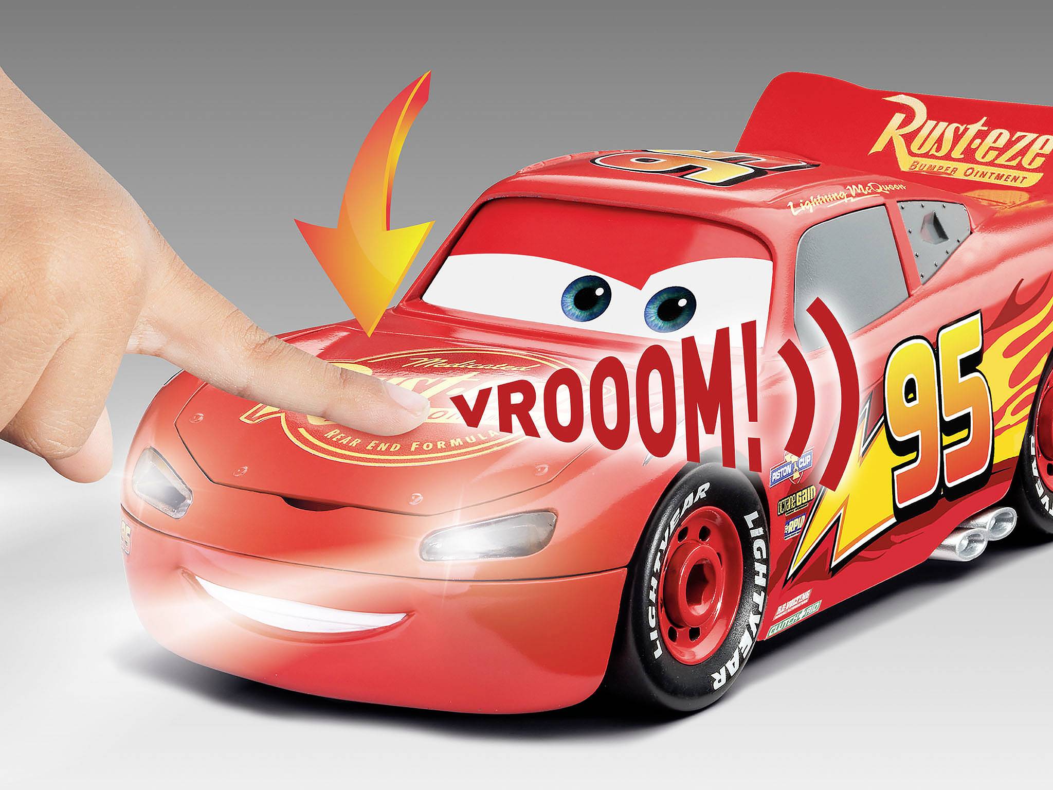 Ein rotes Spielzeugauto mit der Nummer '95' und einem lächelnden Gesicht. Ein Finger drückt darauf, wodurch ein 'Vrooom!'-Geräusch entsteht.