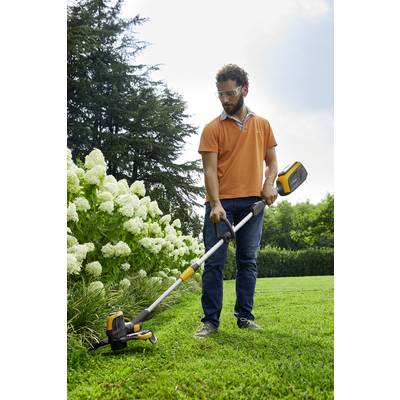 Ein Mann in einem orangefarbenen Hemd trimmt mit einem elektrischen Rasentrimmer das Gras neben weißen Blüten in einem Garten.