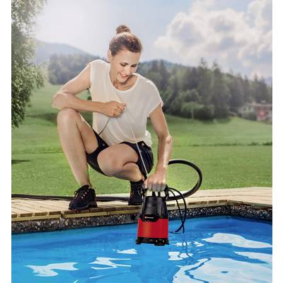 Eine Person kniet am Rand eines Pools und bedient eine Tauchpumpe, um Wasser abzupumpen. Im Hintergrund ist eine grüne Wiese.