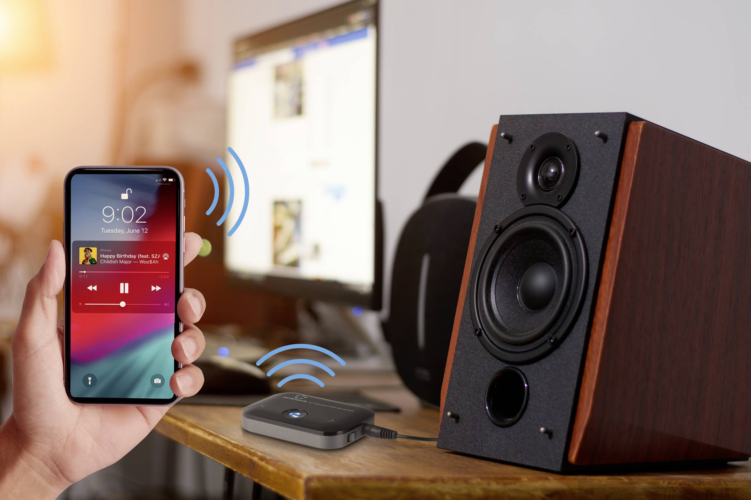 Ein Smartphone verbindet sich drahtlos mit einem Lautsprecher. Im Hintergrund sind unscharfe Computerbildschirme sichtbar.