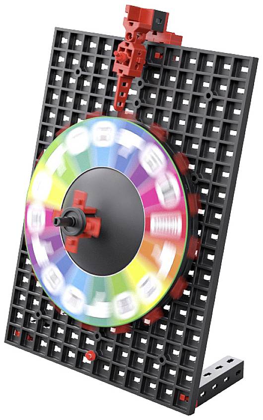 Ein bunter Kreisel mit Buchstaben auf einem schwarzen Gitter, das aufrecht auf einem Tisch steht.