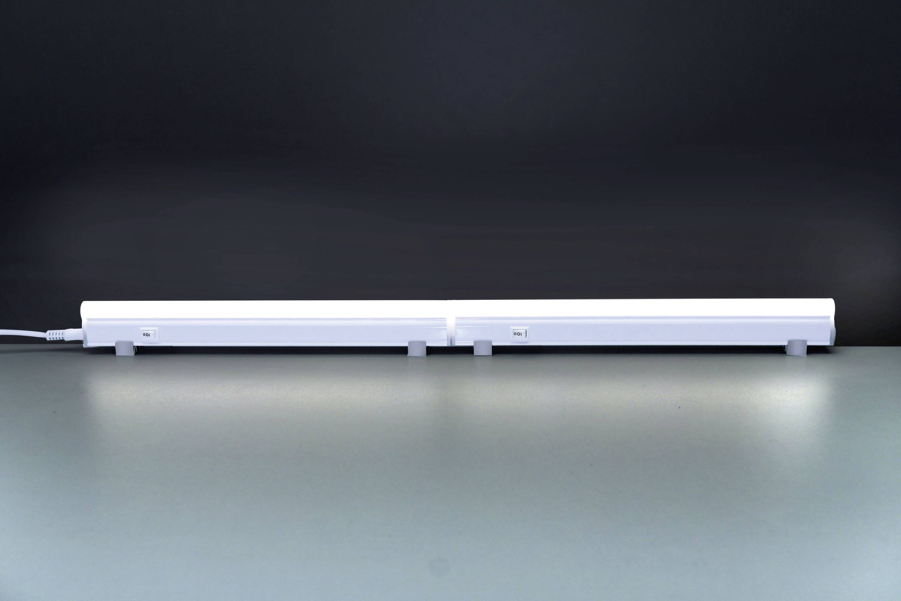 Ein langer, weißer LED-Lichtstab liegt auf einem Tisch vor einem dunklen Hintergrund. Er ist in der Mitte geteilt und hat ein Kabel links.