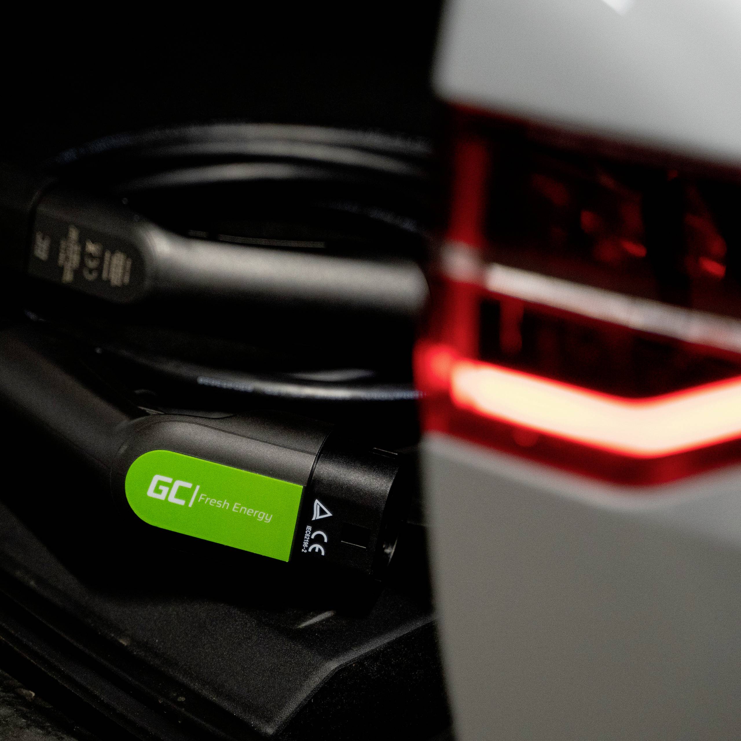 Nahaufnahme eines Elektroauto-Ladekabels, das an einem Fahrzeuganschluss angeschlossen ist. Kabel mit grünem Label 'GC Fresh Energy'.