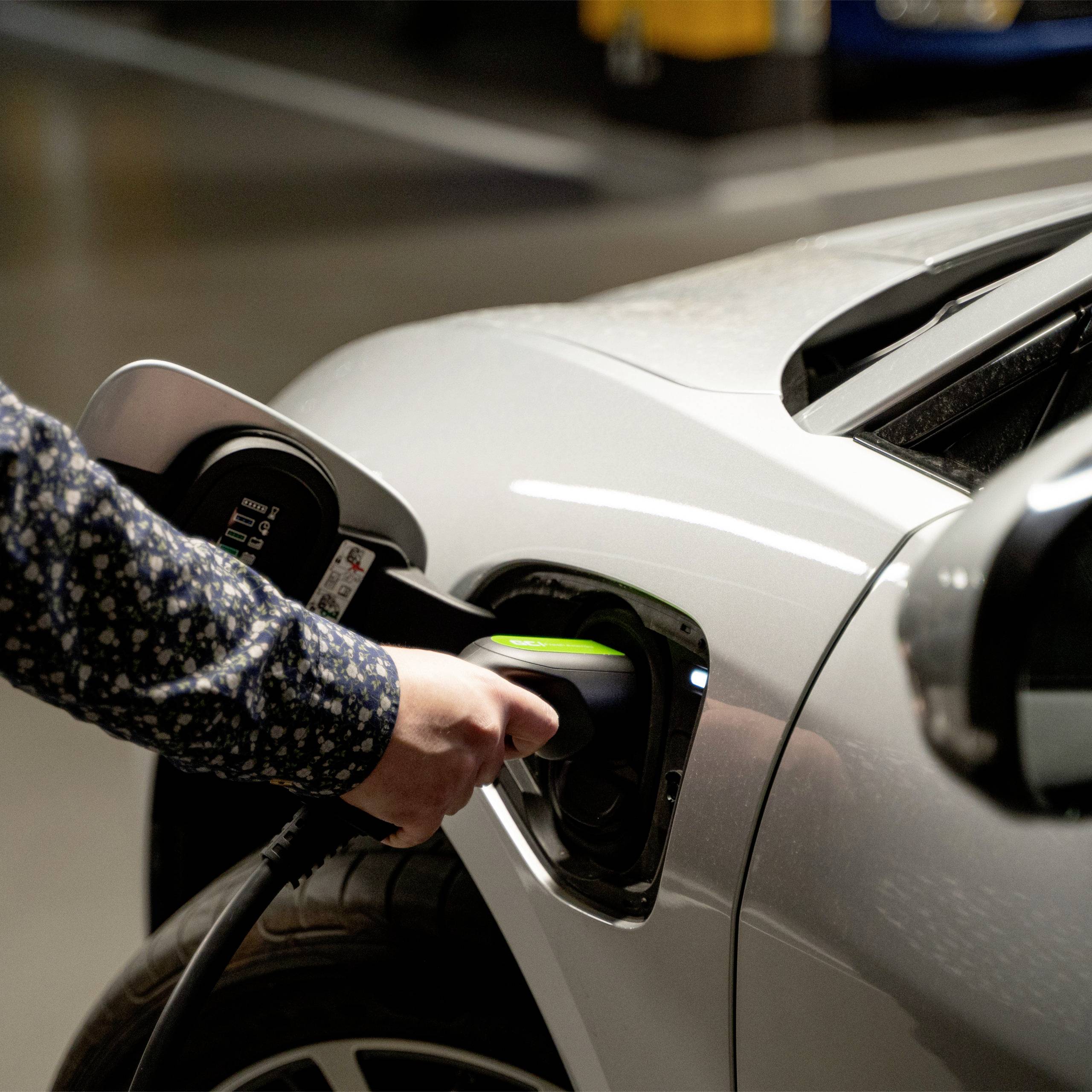 Person lädt ein Elektrofahrzeug in einer Tiefgarage. Der Ladeanschluss ist an der Vorderseite des Autos angebracht.