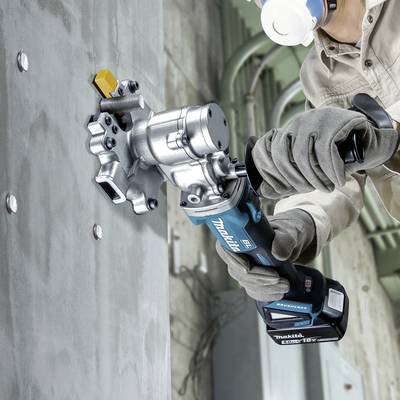 Ein Arbeiter trägt eine Schutzmaske und Handschuhe und nutzt eine blaue elektrische Bohrmaschine, um ein Metallstück an einer Betonwand zu befestigen.