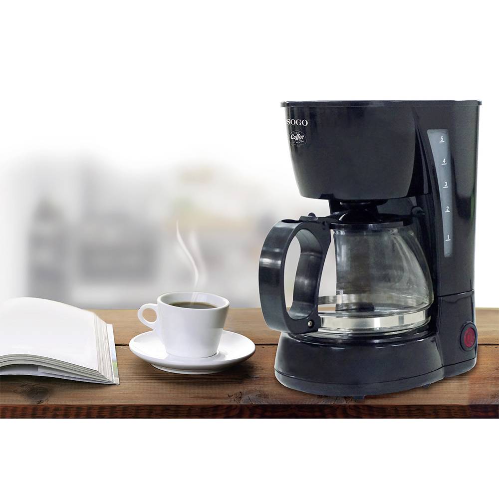 Kaffeemaschine mit Glaskanne und Tassen auf Holztheke, daneben ein aufgeschlagenes Buch; gemütliche Küchenszene.