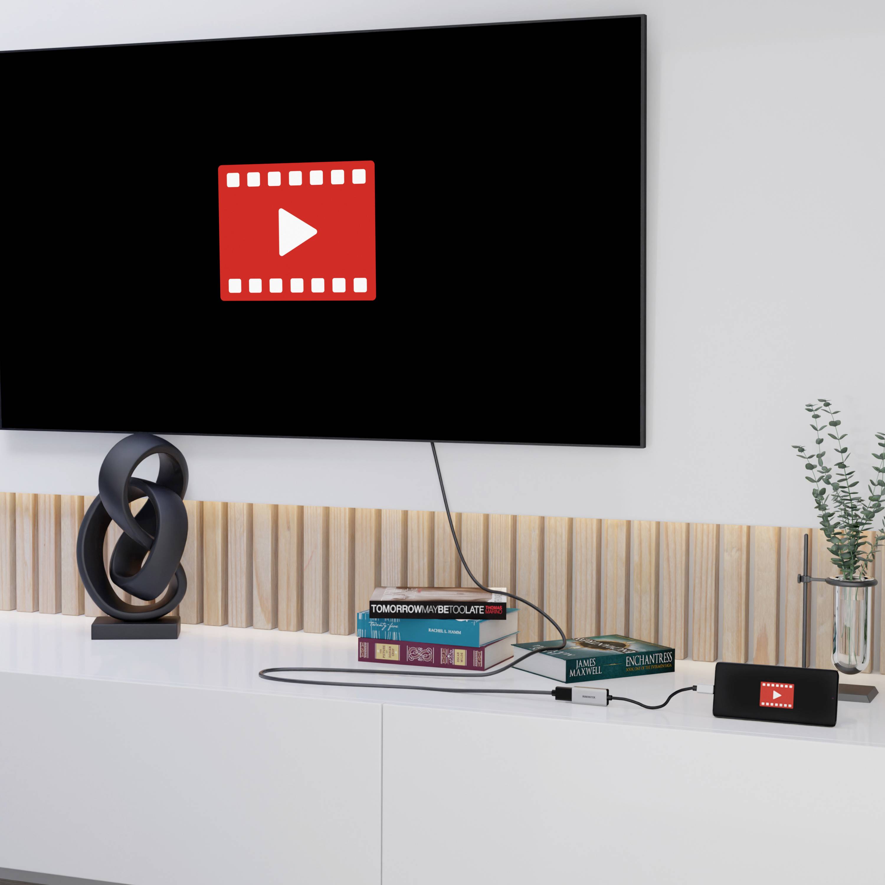 Ein Fernseher und ein Smartphone zeigen das Symbol einer Filmklappe mit einem Play-Button. Daneben steht eine Pflanze auf einem weißen Schrank.