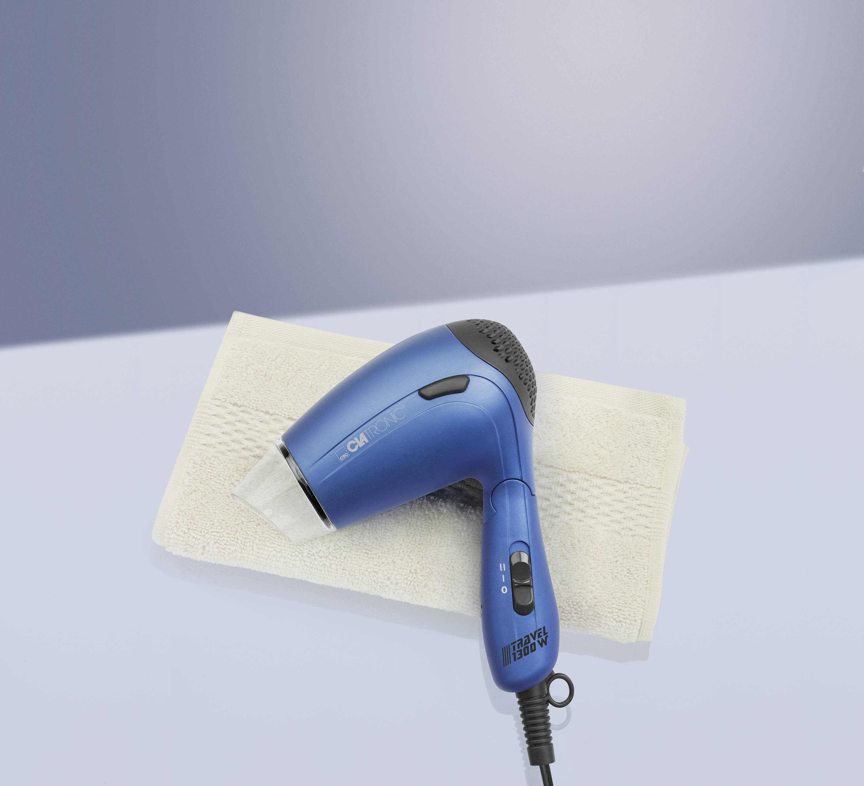 Ein blauer Haartrockner liegt auf einem beigen Handtuch vor einem neutralen Hintergrund. Der Haartrockner hat schwarze Details.