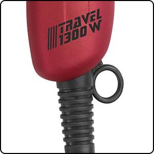 Ein rotes Gerät mit der Aufschrift 'TRAVEL 1300 W'. Der Griff hat eine runde Schlaufe. Hauptsächlich für Reiseanwendungen geeignet.