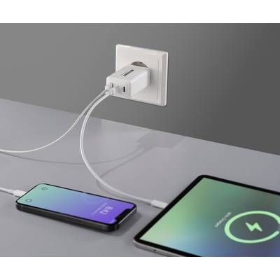 Ein Ladeadapter steckt in einer Steckdose und lädt gleichzeitig ein Smartphone und ein Tablet. Beide Geräte zeigen Ladebildschirme an.
