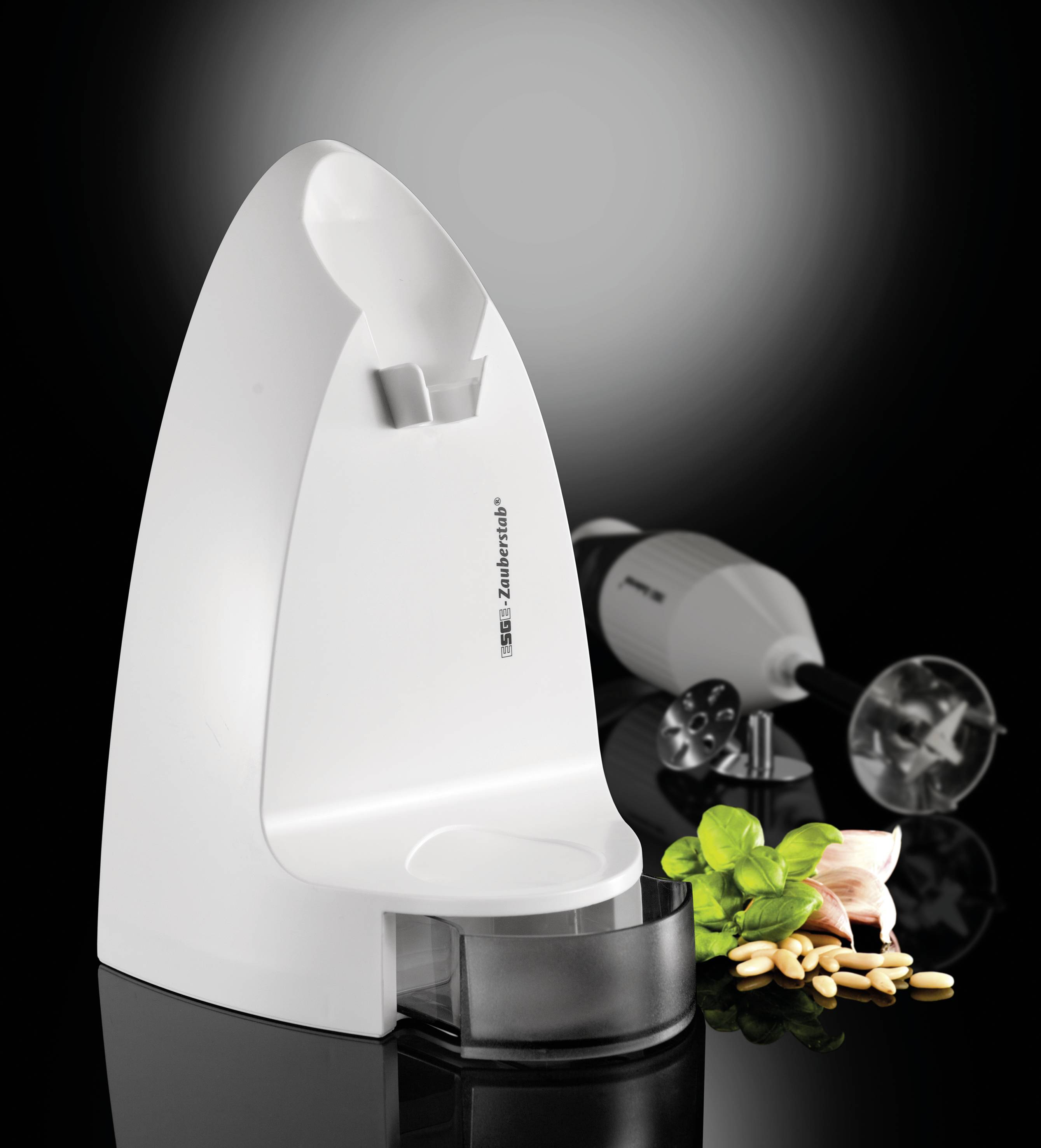 Ein weißer, moderner automatischer Seifenspender vor einem schwarzen Hintergrund. Daneben ein Stabmixer mit Minze, Knoblauch und Pinienkernen.