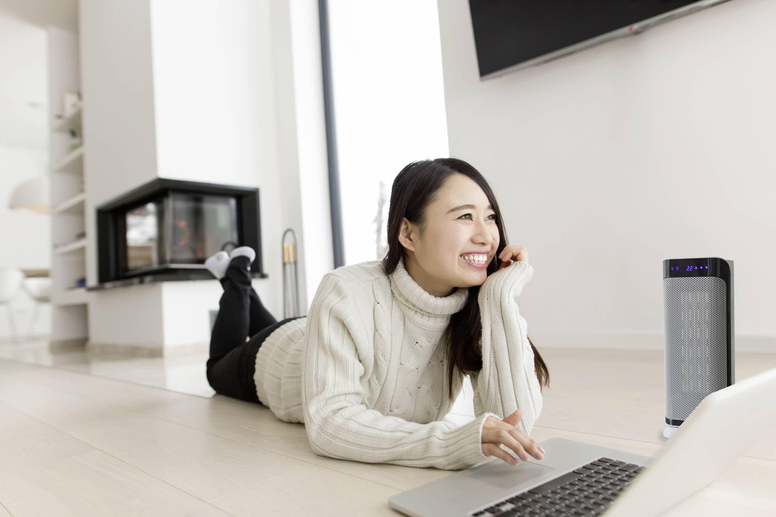 Eine lächelnde Person liegt auf dem Boden, arbeitet am Laptop und hat einen Luftreiniger daneben im Raum.