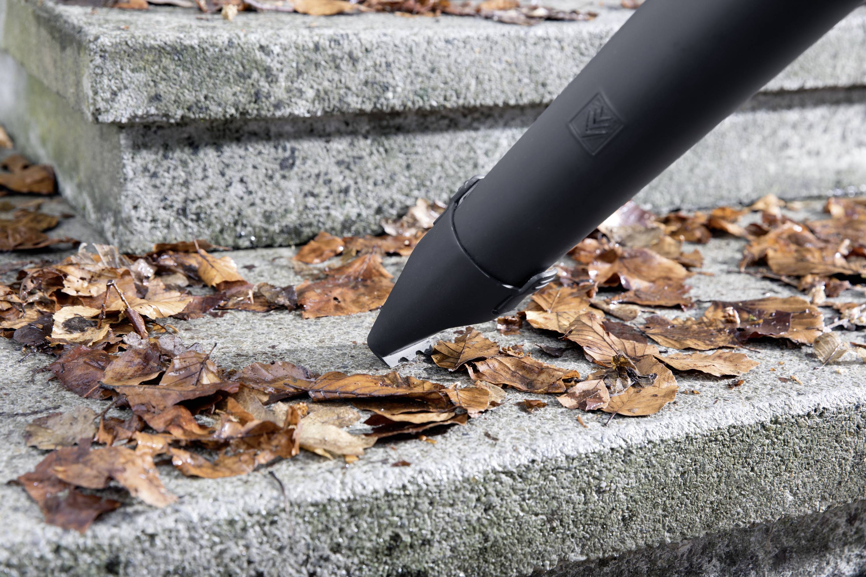 Ein Laubbläser pustet trockene, braune Blätter von einer Treppe weg. Die Treppe besteht aus grauem Stein.