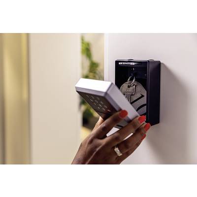Eine Hand öffnet ein elektronisches Türschloss mit einem Zahlenfeld, um einen Schlüsselkasten mit einem Schlüsselbund darin freizulegen.