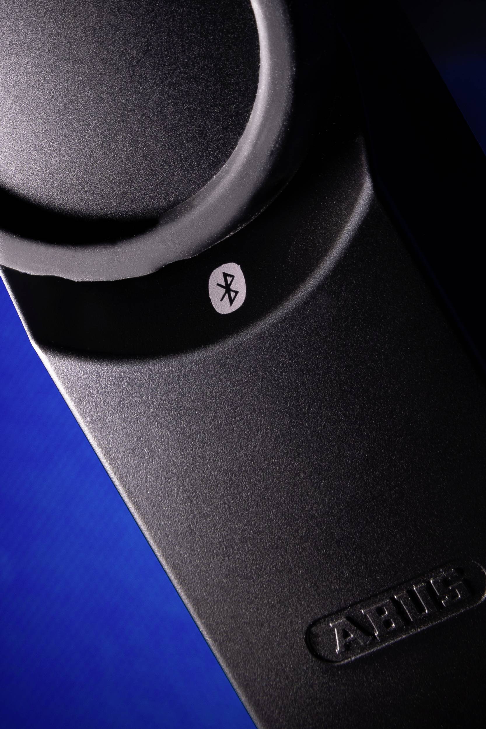 Schwarzes technisches Gerät mit Bluetooth-Symbol auf einer blauen Oberfläche, Logo eingeprägt.