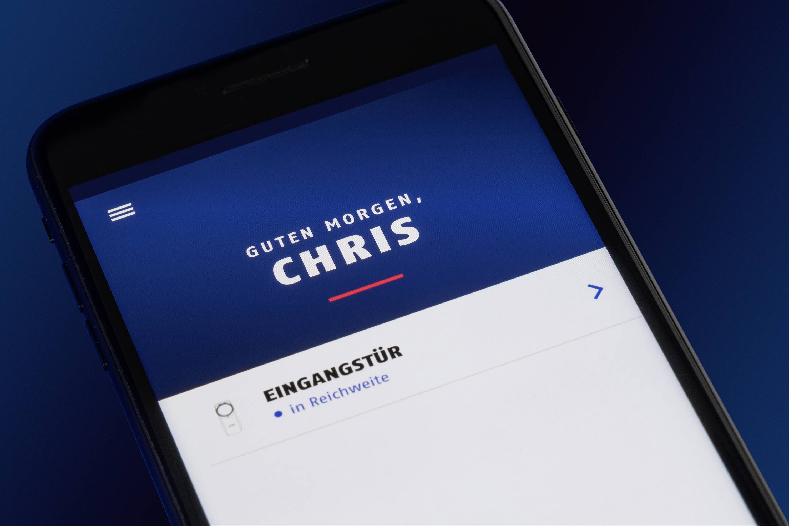 Smartphone-Display zeigt eine Begrüßung 'Guten Morgen, Chris' mit einer Benachrichtigung über die Eingangstür, die in Reichweite ist.
