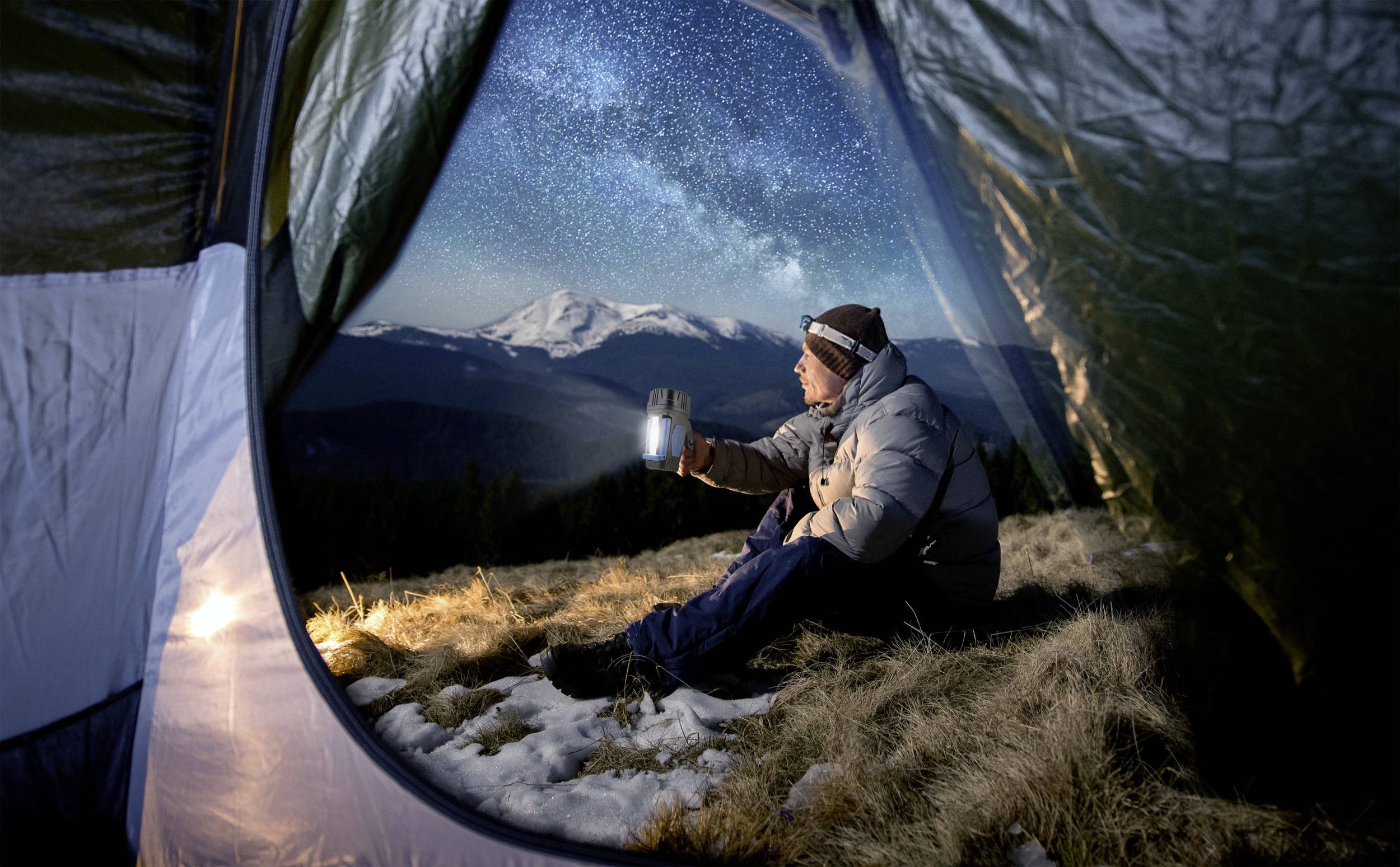 Person sitzt im Zelt, genießt die Aussicht auf schneebedeckte Berge und Sternenhimmel. Die Szene vermittelt Ruhe und Naturverbundenheit.