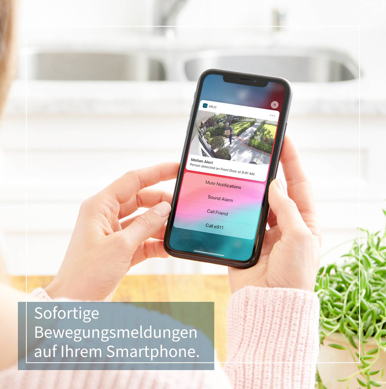 Eine Hand hält ein Smartphone mit einer Benachrichtigung zur Bewegungserkennung. Text: 'Sofortige Bewegungsmeldungen auf Ihrem Smartphone.' Pflanzen im Vordergrund.