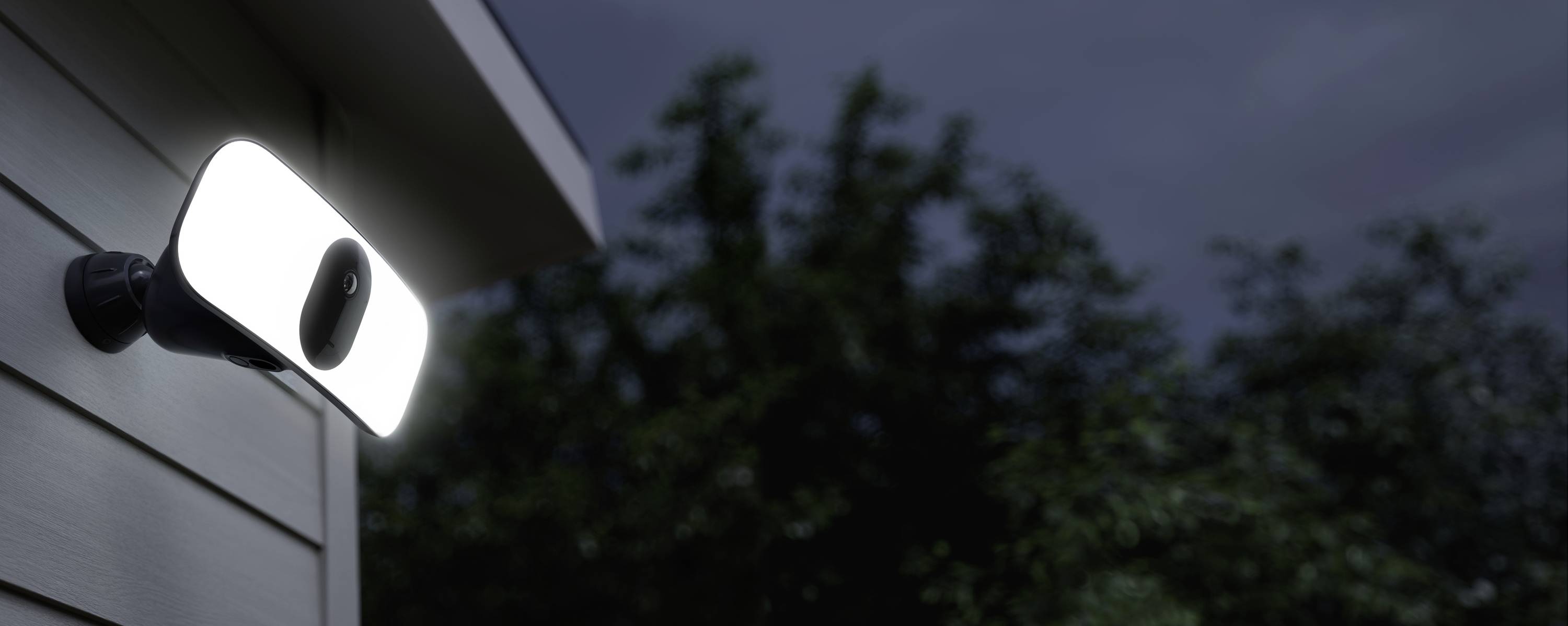 Eine Außenkamera mit integriertem Flutlicht ist an einem Haus angebracht, beleuchtet eine dunkle Umgebung bei Nacht.