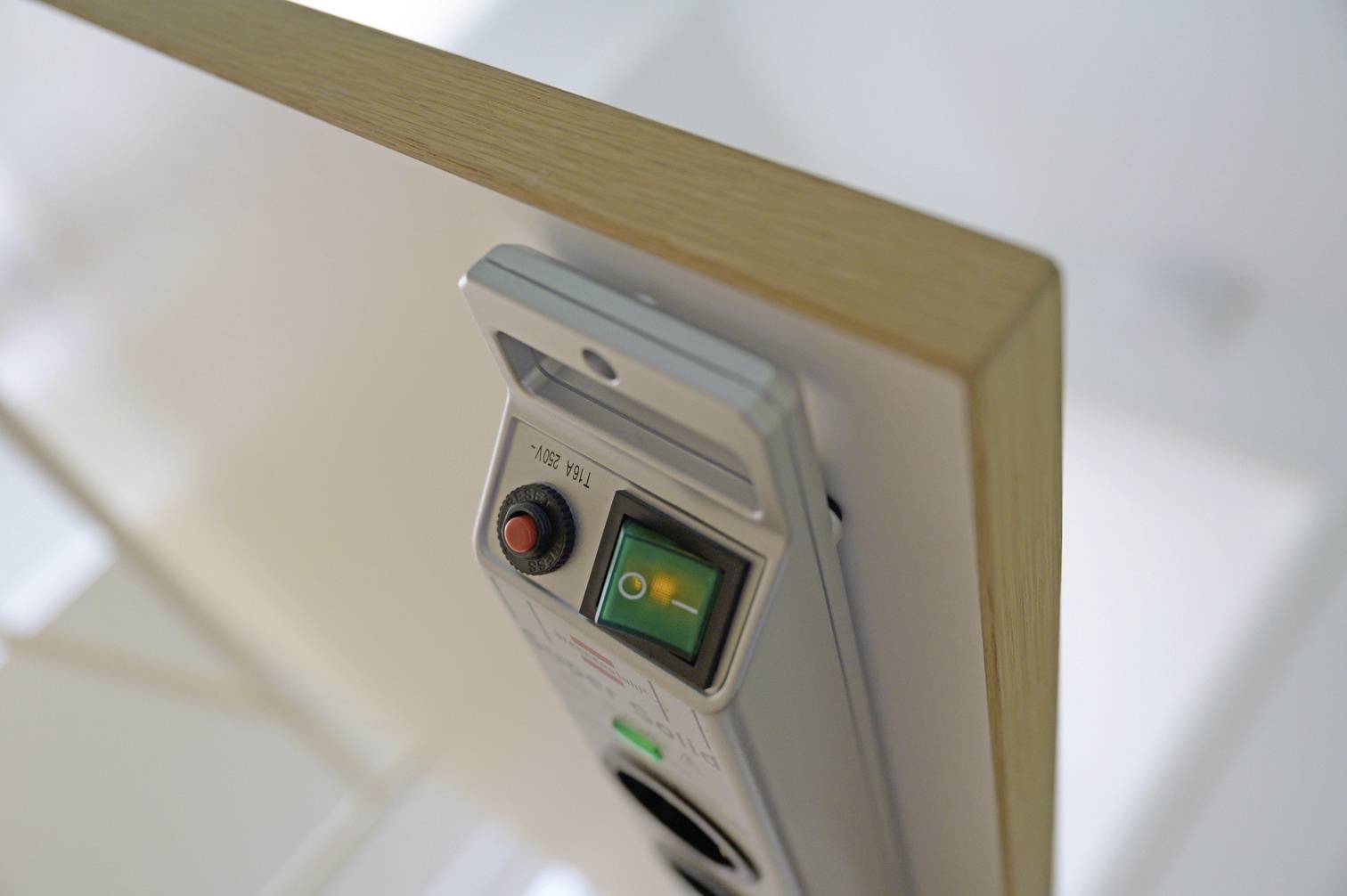 Ein silberner Lichtschalter mit integriertem grünen Kippschalter und rotem Knopf an einer Holzkante montiert.