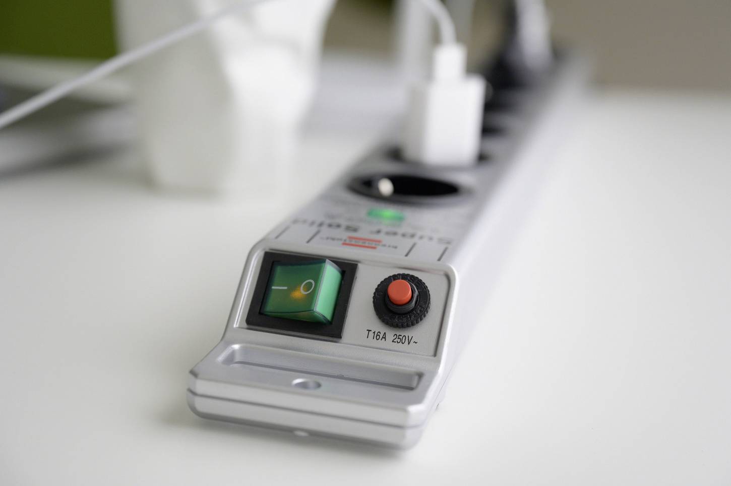 Eine silberne Mehrfachsteckdose mit sechs Anschlüssen, einem grünen Kippschalter und einem USB-Netzteil, das angeschlossen ist.