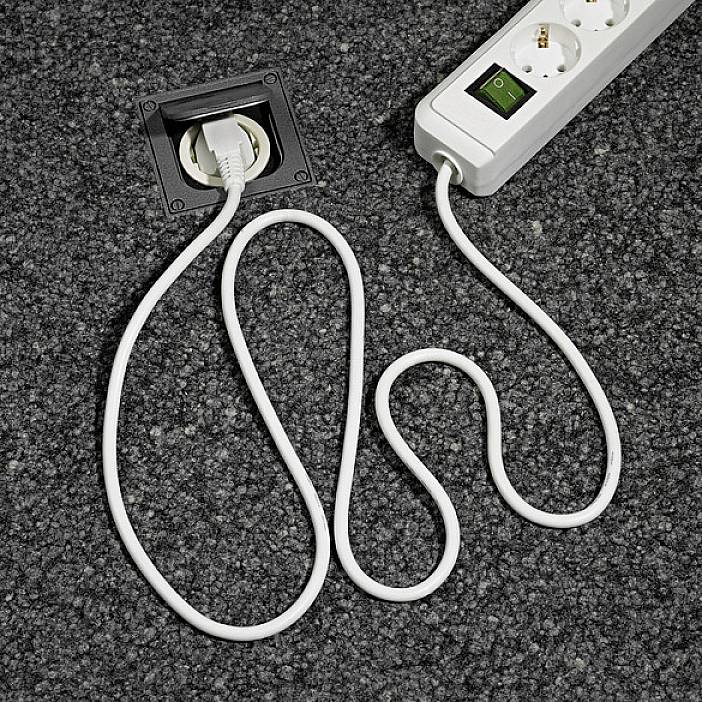 Ein verlängerungskabel mit Schalter liegt auf einem grauen Teppich. Ein Stecker ist in die Leiste eingesteckt.