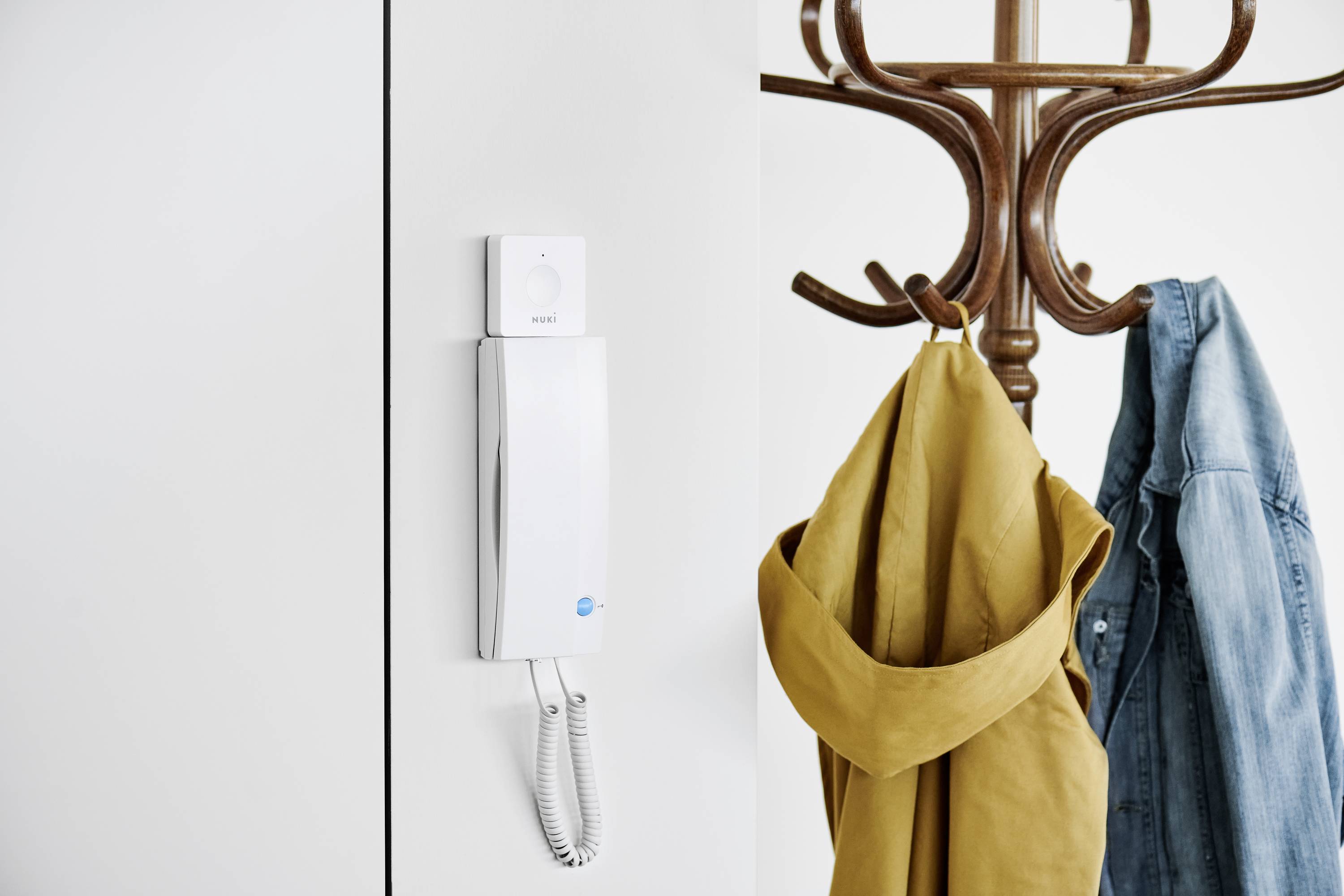 Telefon an Wand neben einem Garderobenständer mit gelbem Mantel und Jeansjacke.