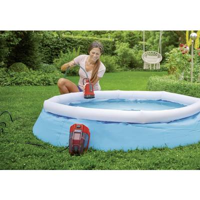 Eine Frau entleert ein kleines blaues Schwimmbecken mit einer Pumpe. Der Garten im Hintergrund ist grün und üppig.